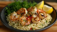 Grilled shrimp with herbs served over pasta noodles in cast iron skillet with lemon wedges and fresh parsley garnish on wooden table background.