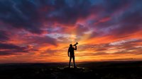 Silhouette of a man standing on a rock with a megaphone against a dramatic fiery sunset sky, symbolizing leadership and announcement.