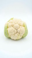 Fresh whole cauliflower with pale green leaves isolated on white background, suitable for food, nutrition, cooking, and healthy eating concepts.