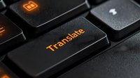 Black keyboard with illuminated orange translate button in dark setting, macro photography showing textured keycaps and backlit text.