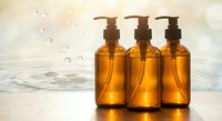 Three amber glass pump bottles with golden liquid soap or oil arranged on wet surface with water droplets and ripples for spa and wellness skincare routine.