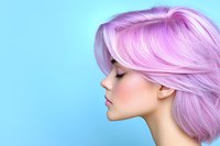 Young Caucasian woman with pink pastel hair in profile view against blue background, showcasing modern hair coloring and styling trends in beauty industry.