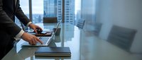 Professional businessman working on laptop in modern office conference room with city skyline view through windows for corporate presentations.