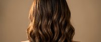 Young woman with long wavy brown hair from behind showing healthy hair texture and natural highlights for beauty and haircare concepts.
