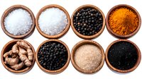 Aromatic spices and seasonings in wooden bowls arranged in rows, including sea salt, black peppercorns, turmeric powder, ginger root, and black seeds.