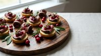 Elegant appetizers with cranberry sauce on crackers arranged on wooden board, garnished with fresh herbs and berries for holiday entertaining.