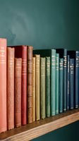 Row of vintage books with colorful spines arranged on wooden shelf against teal wall creating cozy library atmosphere for home decor and reading spaces.