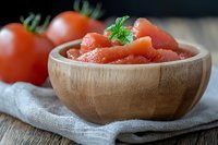 Fresh diced tomatoes in wooden bowl with whole tomatoes and herbs on rustic linen napkin and wooden table, selective focus on foreground.