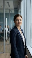 Confident middle-aged Caucasian businesswoman in navy suit standing by office window with modern workplace background for corporate communications.