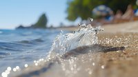 Ocean wave splashing on sandy beach shore with sparkling water droplets and bokeh effect in sunlight, blurred beach and trees background creates serene summer mood.