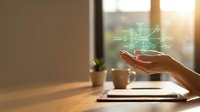 Hand holding holographic digital network connection above laptop on wooden desk with coffee cup and plant in warm sunlight for business technology concepts.