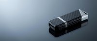 Black carbon fiber USB flash drive with metallic accents on reflective surface for technology and data storage concepts.