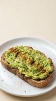 Avocado toast on whole grain bread with spices and seeds served on white plate for healthy breakfast or brunch meal concept.