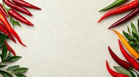 Fresh red and yellow chili peppers with green leaves arranged as frame border on light linen textile background, copy space in center for text.
