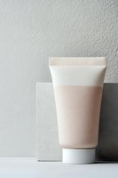 Minimalist cosmetic tube with pink cream against geometric concrete blocks on white surface, modern skincare packaging design composition with soft natural lighting.