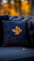 Navy blue decorative cushion with golden maple leaf embroidery and scattered dot pattern on dark sofa, autumn mood with blurred warm background.