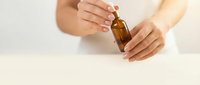 Woman hands holding brown glass dropper bottle for essential oil or serum on neutral background for skincare and wellness routine.