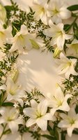 White lily flowers with green foliage arranged in elegant floral frame composition on soft beige background for wedding invitations and spring decorations.