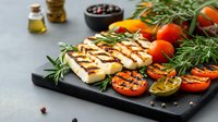 Grilled halloumi cheese with charred tomatoes and fresh rosemary on black stone board, mediterranean ingredients and olive oil for healthy cooking.