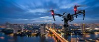 Professional drone flying over illuminated city skyline at dusk with glowing lights and urban waterfront for aerial photography and videography projects.