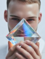 Young Caucasian man holding crystal prism creating rainbow light refraction effects. Science, optics, physics education and light spectrum demonstration concept.