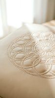 Close-up of cream quilted mattress surface with intricate circular stitching pattern in soft natural bedroom lighting for comfort and sleep concepts.