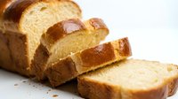 Fresh baked brioche bread loaf sliced on white background showing golden crust and soft fluffy texture perfect for breakfast sandwiches and toast.