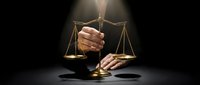 Professional businessman holding golden scales of justice in dramatic spotlight representing legal balance, fairness and judicial decision making.