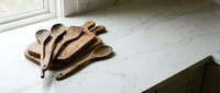 Handcrafted wooden spoons collection on marble surface near window with natural lighting for kitchen utensils and cooking accessories display.
