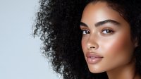 Young African American woman with natural curly hair and glowing skin looking at camera with confident expression against neutral background for beauty and skincare concepts.