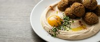 Creamy hummus topped with olive oil and fresh herbs served with crispy falafel balls on white plate, traditional Middle Eastern appetizer for restaurants.