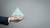 Businessman in suit holding glowing green geometric pyramid hologram, symbolizing innovation, technology, and futuristic business strategy concepts.