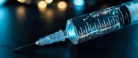 Medical syringe with needle on dark surface with blurred lights background for healthcare and vaccination concepts.