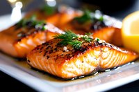 Grilled salmon fillets with caramelized glaze, fresh dill garnish and citrus on white plate. Close up of moist, flaky fish with golden-brown seared surface.