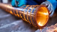 Glowing copper pipe with intricate spiral pattern being processed in metalworking shop, bright orange heat emanating from inside during industrial manufacturing process.