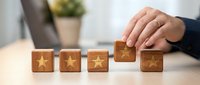 Hand placing wooden cube with golden star among four star blocks on desk representing customer satisfaction rating and quality service evaluation.