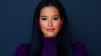 Young Asian woman with long black hair wearing purple turtleneck sweater smiling confidently against dark blue background, professional studio portrait with soft lighting.