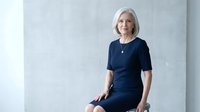 Professional mature Caucasian businesswoman in navy dress sitting confidently in modern office environment for corporate headshots and business marketing.