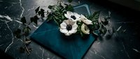 Elegant white anemone flowers arranged on teal velvet envelope against dark marble surface for luxury wedding invitations and romantic stationery design.