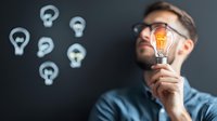 Young Caucasian businessman in glasses holding glowing lightbulb against dark background with light bulb icons. Concept of creative business solutions and innovation.