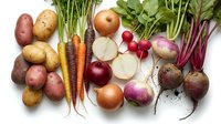 Fresh organic root vegetables and leafy greens arranged on white background including potatoes, carrots, onions, radishes, turnips and beets for healthy cooking.