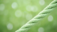 Diagonal green rope against blurred bokeh background creates minimalist composition with soft natural lighting and shallow depth of field.