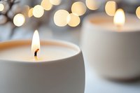 Lit white candles in ceramic holders with warm bokeh lights in background, creating cozy ambiance for home decor, relaxation, spa, and holiday celebrations.