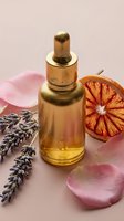 Luxury golden serum bottle with dropper surrounded by dried lavender, orange slice and pink rose petals on soft pink background for skincare and aromatherapy.