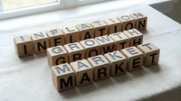 Wooden letter blocks spelling inflation growth market on white surface near window. Business economics finance concept for presentations and educational materials.