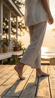 Woman walking barefoot on wooden deck in linen outfit during golden hour sunset, relaxed summer lifestyle and wellness concept for vacation retreat.