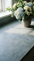 Elegant floral arrangement with blue hydrangeas and white roses in ceramic vase on marble windowsill creating sophisticated home decor atmosphere.