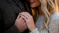 Close-up of engaged couple holding hands showing diamond engagement ring on woman's finger against dark suit jacket for wedding planning.