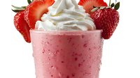 Fresh strawberry milkshake topped with whipped cream and garnished with sliced strawberries in frosty glass with water droplets on white background.