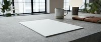 Blank white paper sheet on modern concrete desk with coffee mug and notebook in bright office workspace for business presentations and creative projects.